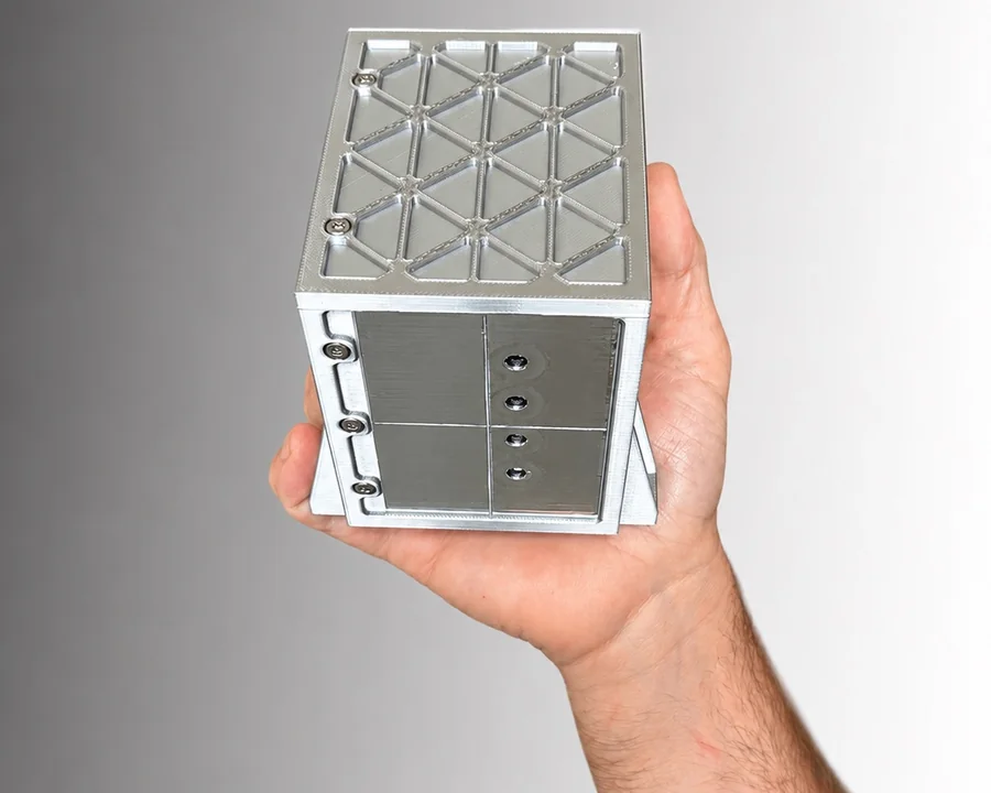 A hand holding the GIAN engineering model, a milled aluminium cube of 10 centimetres